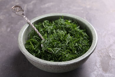 Photo of Fresh cut dill and spoon in bowl on grey textured table, closeup