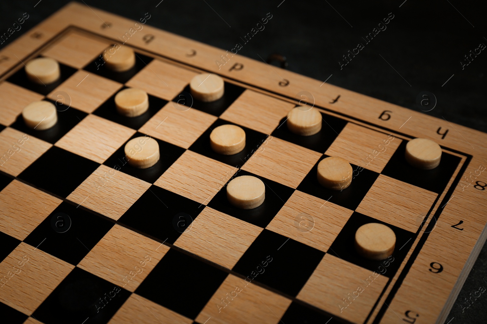 Photo of Wooden checkerboard with game pieces on black table, closeup