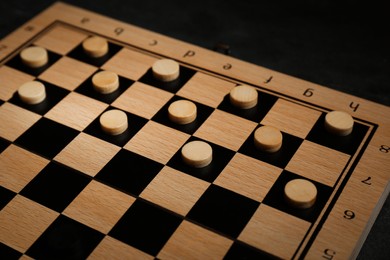 Photo of Wooden checkerboard with game pieces on black table, closeup