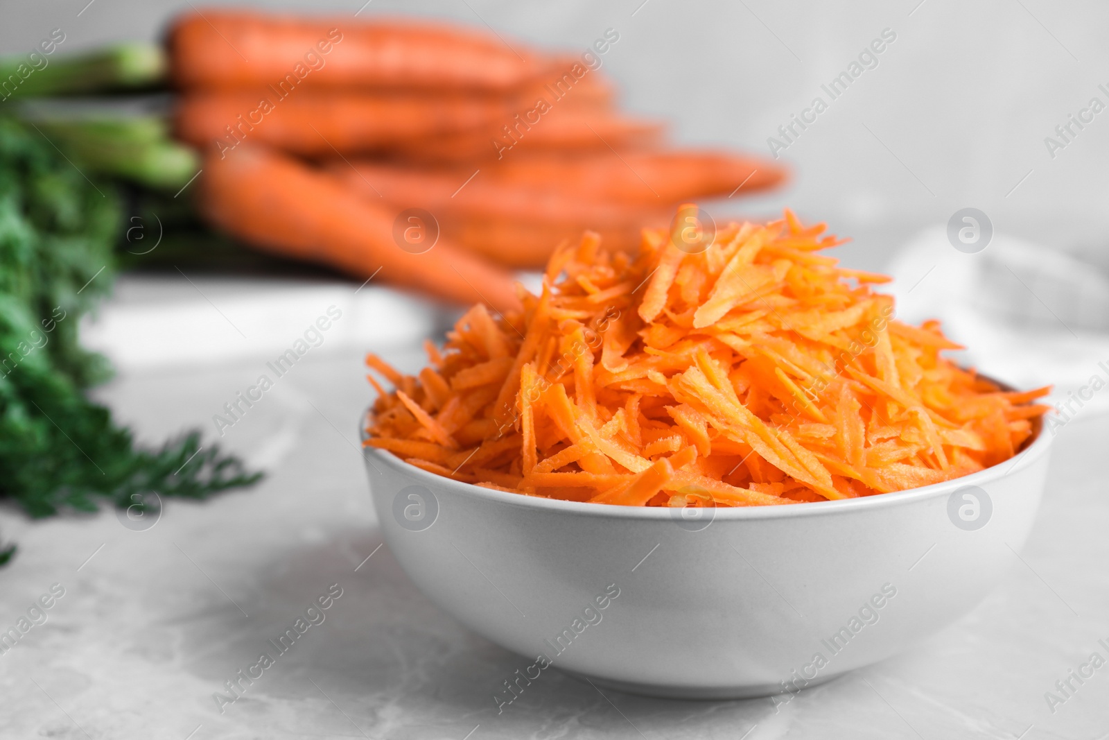 Photo of Grated carrot in bowl on light grey marble table, closeup