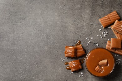 Tasty salted caramel with candies in glass bowl on grey table, flat lay. Space for text