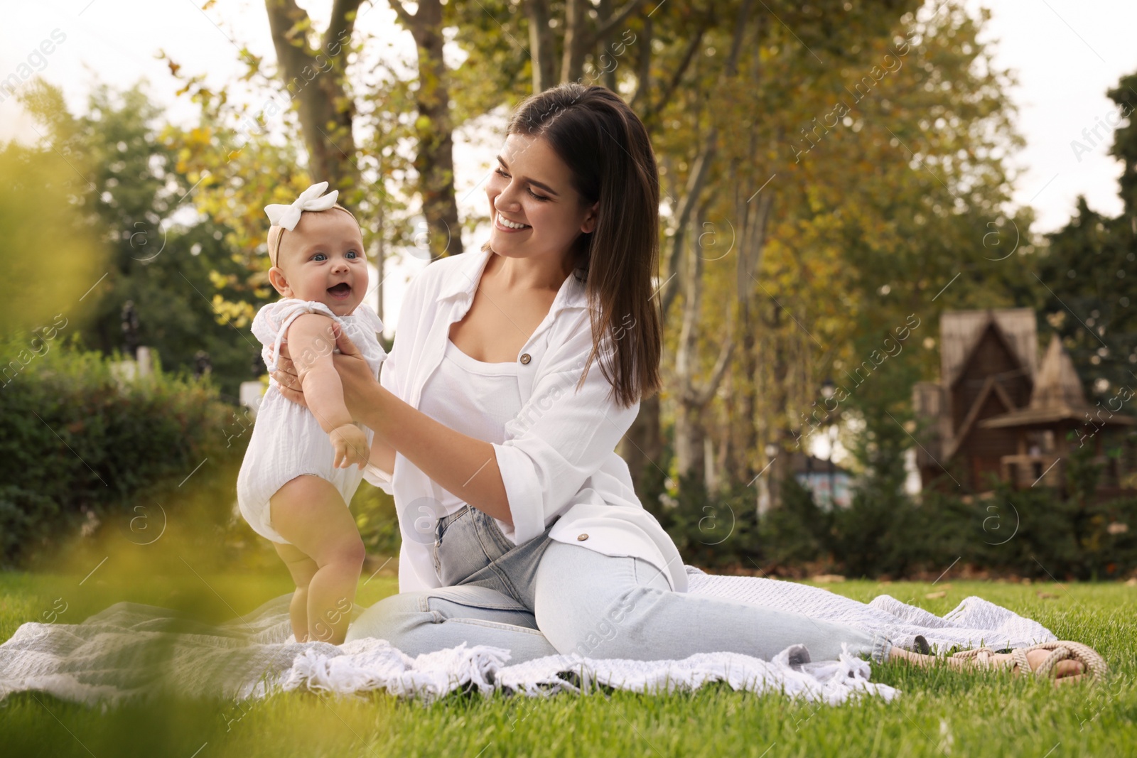 Photo of Happy mother with adorable baby sitting on green grass in park