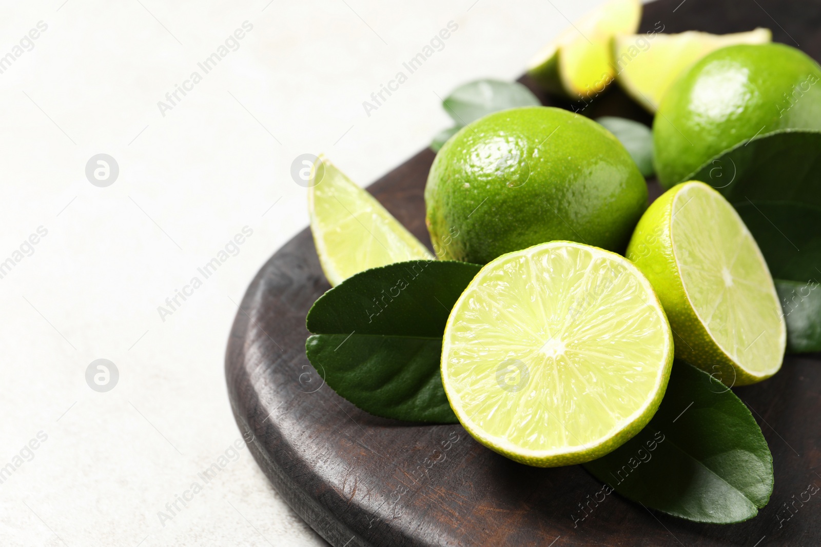Photo of Fresh ripe limes and green leaves on light table, closeup. Space for text