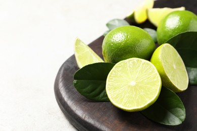 Photo of Fresh ripe limes and green leaves on light table, closeup. Space for text