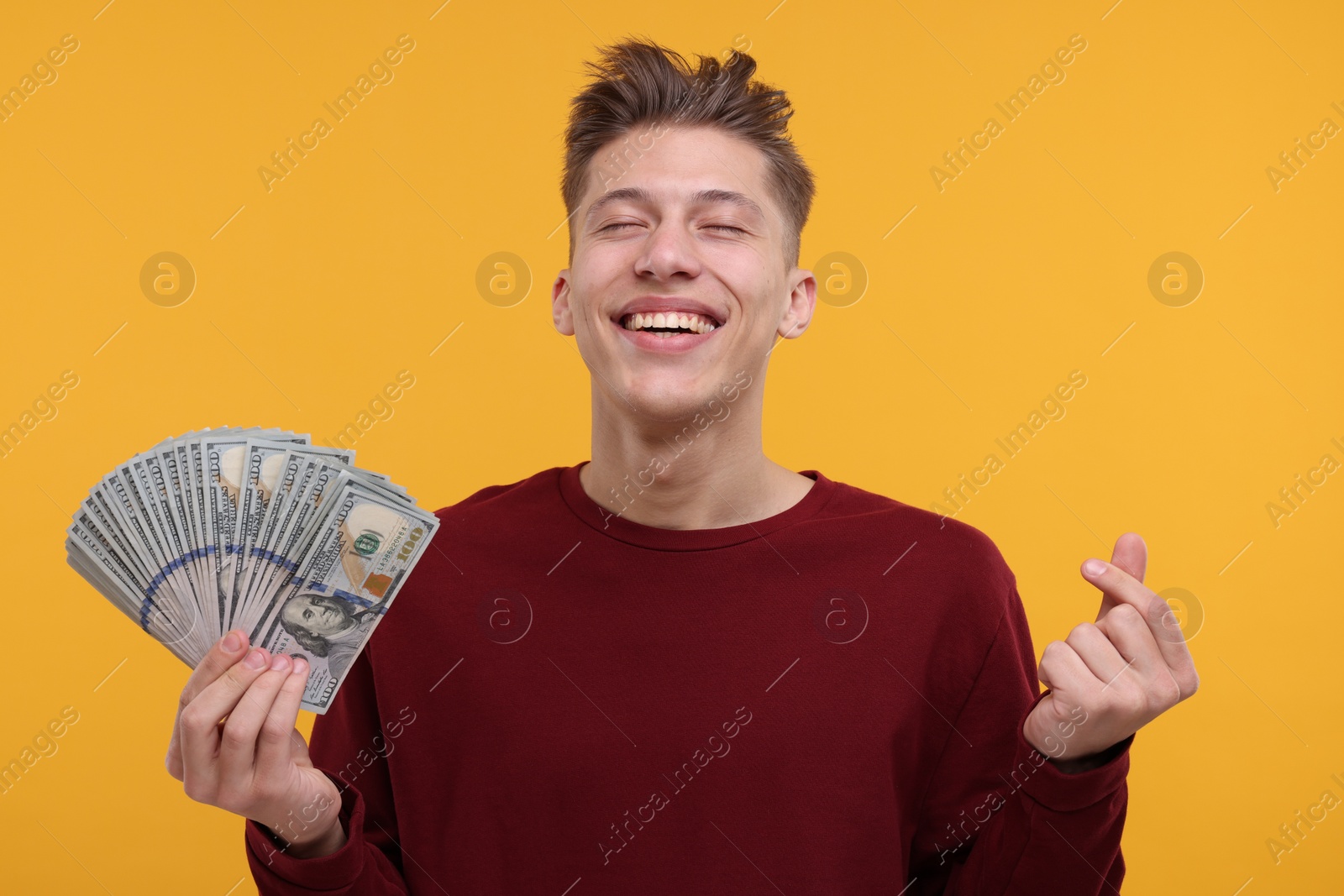 Photo of Happy man with dollar banknotes showing money gesture on yellow background