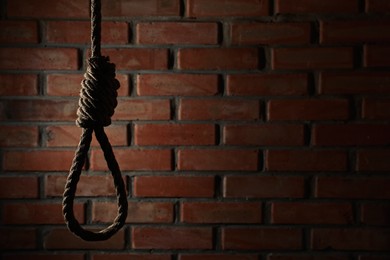 Photo of Rope noose with knot hanging near brick wall, space for text