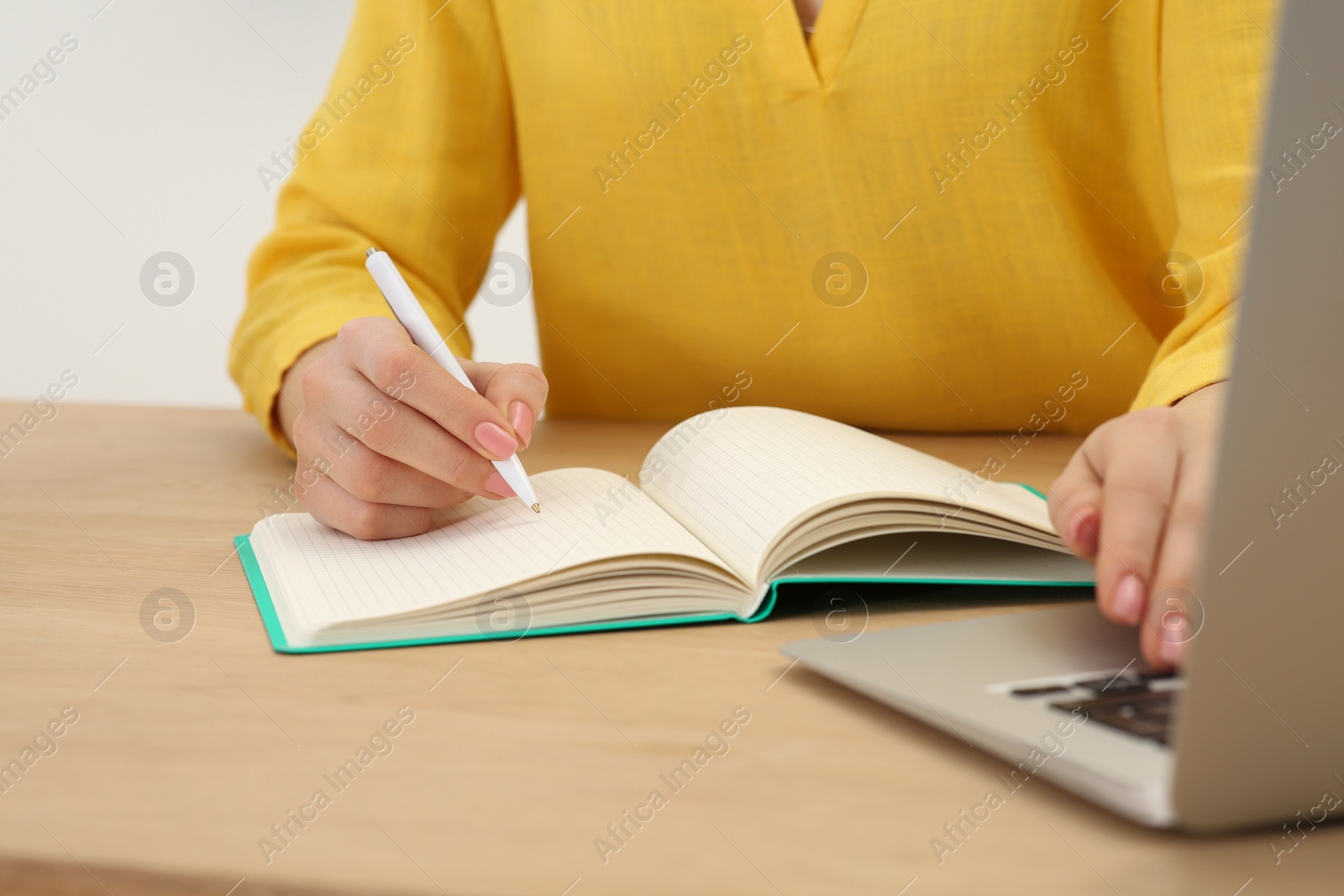 Photo of Woman writing in notebook at wooden table indoors, closeup