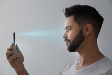 Image of Young man unlocking smartphone with facial scanner on grey background. Biometric verification