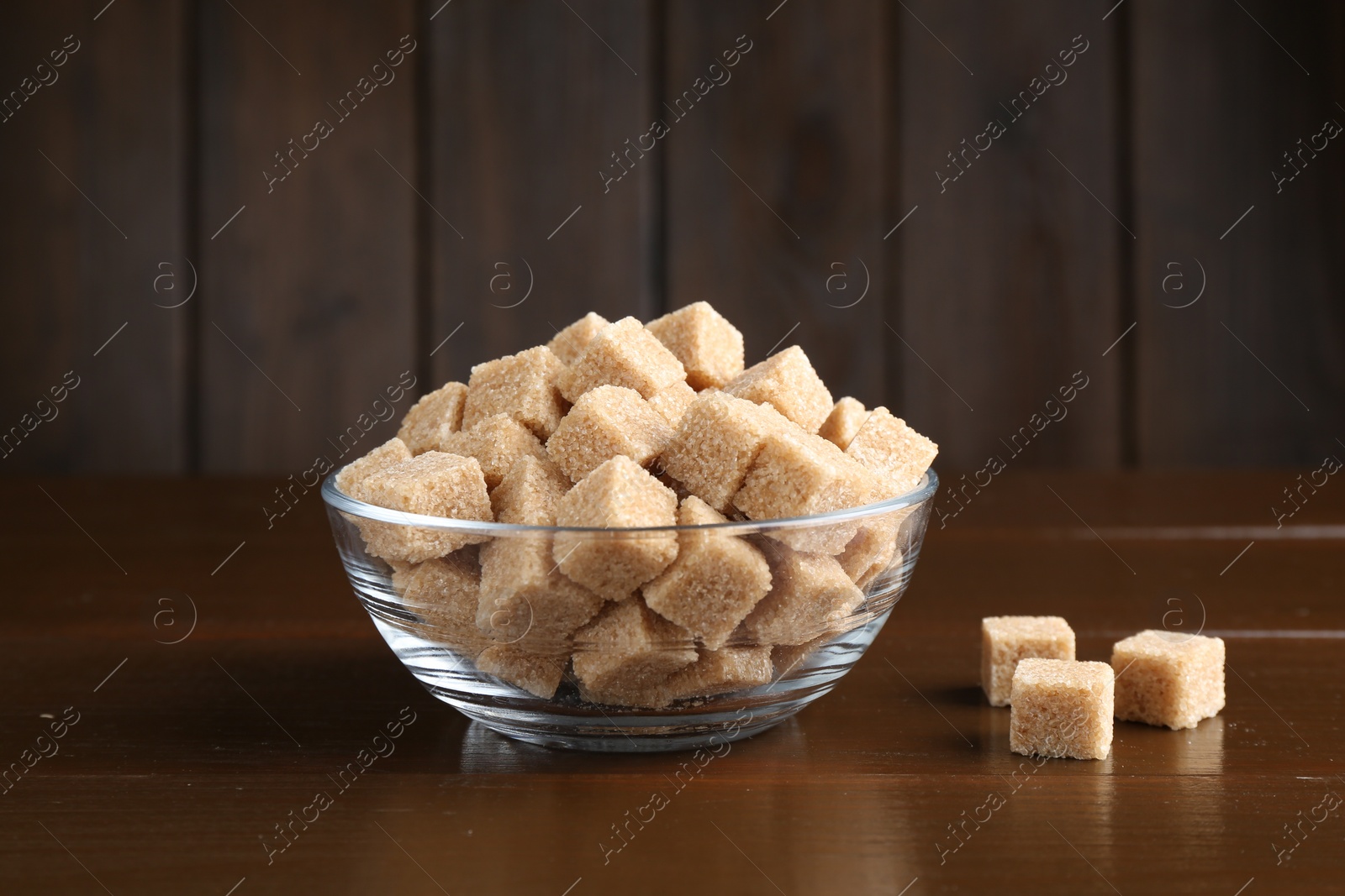 Photo of Brown sugar cubes in glass bowl on wooden table