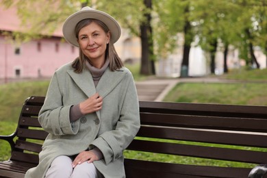 Beautiful senior woman sitting on bench in park, space for text