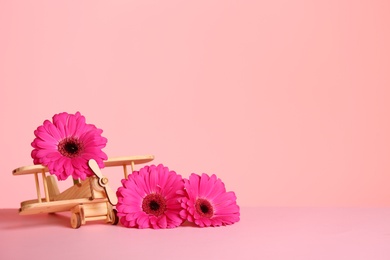 Photo of Wooden plane and flowers on table against color background, space for text. International Women's Day
