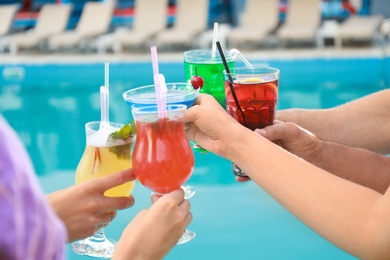 Friends clinking glasses with fresh summer cocktails near swimming pool, closeup