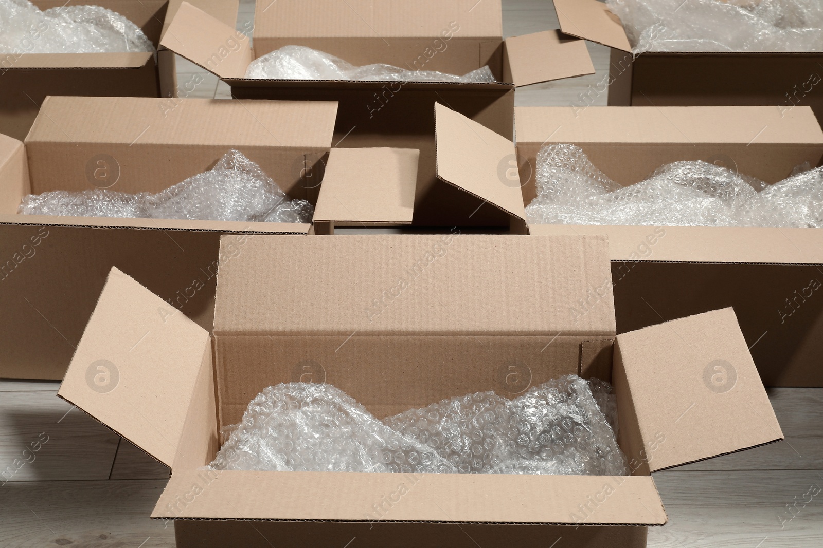 Photo of Many open cardboard boxes with bubble wrap on white wooden floor