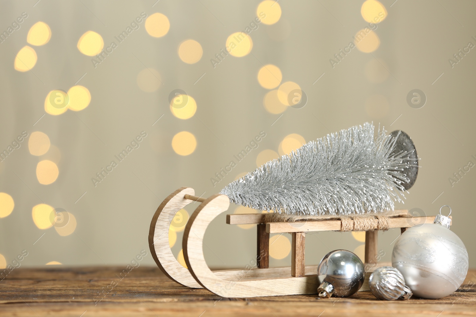 Photo of Decorative sleigh with Christmas tree and balls on wooden table against blurred lights. Space for text