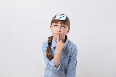 Emotional girl with question mark sticker on forehead against white background