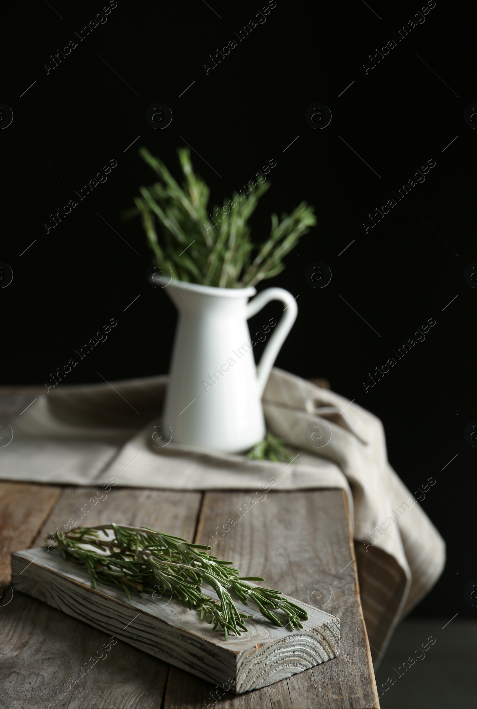 Photo of Wooden board and jug with fresh green rosemary on table. Aromatic herbs