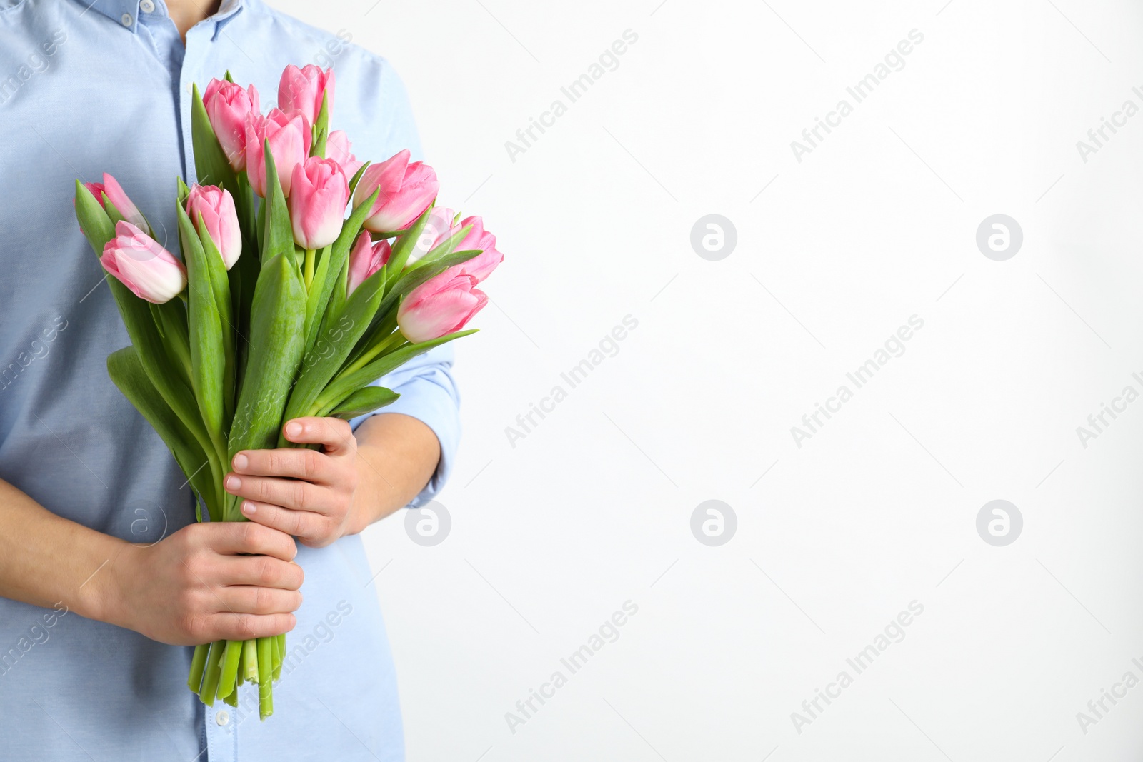 Photo of Man holding bouquet of beautiful spring tulips on light background, closeup. International Women's Day