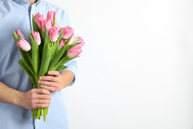 Photo of Man holding bouquet of beautiful spring tulips on light background, closeup. International Women's Day