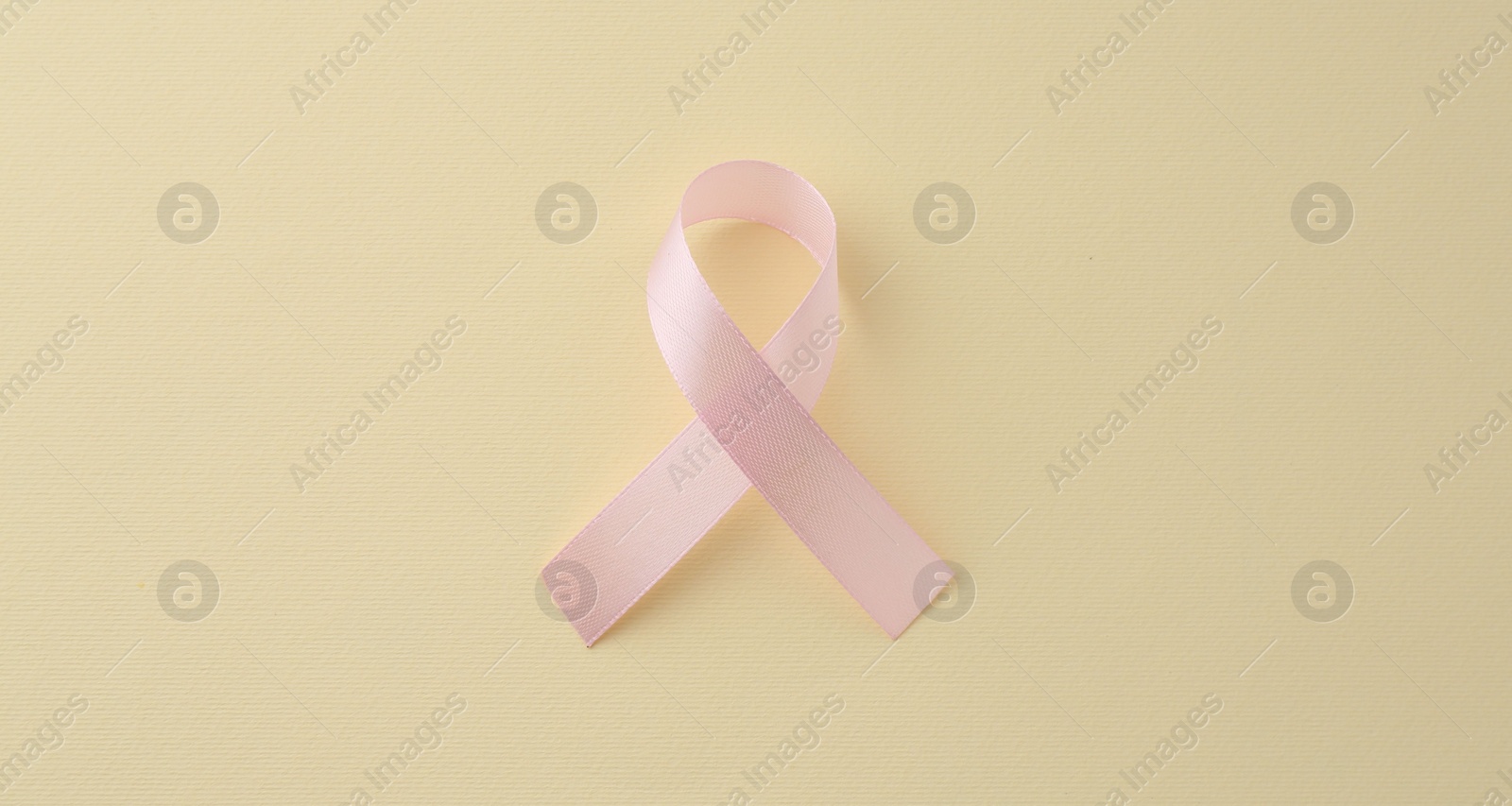 Photo of Pink awareness ribbon on pale yellow background, top view