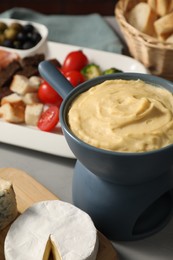 Fondue with tasty melted cheese and different snacks on grey table