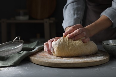 Photo of Woman kneading dough at grey table, closeup