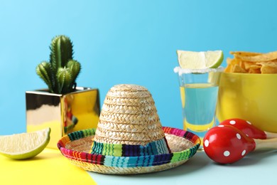 Photo of Mexican sombrero hat, cactus, nachos chips, maracas and tequila on light blue background
