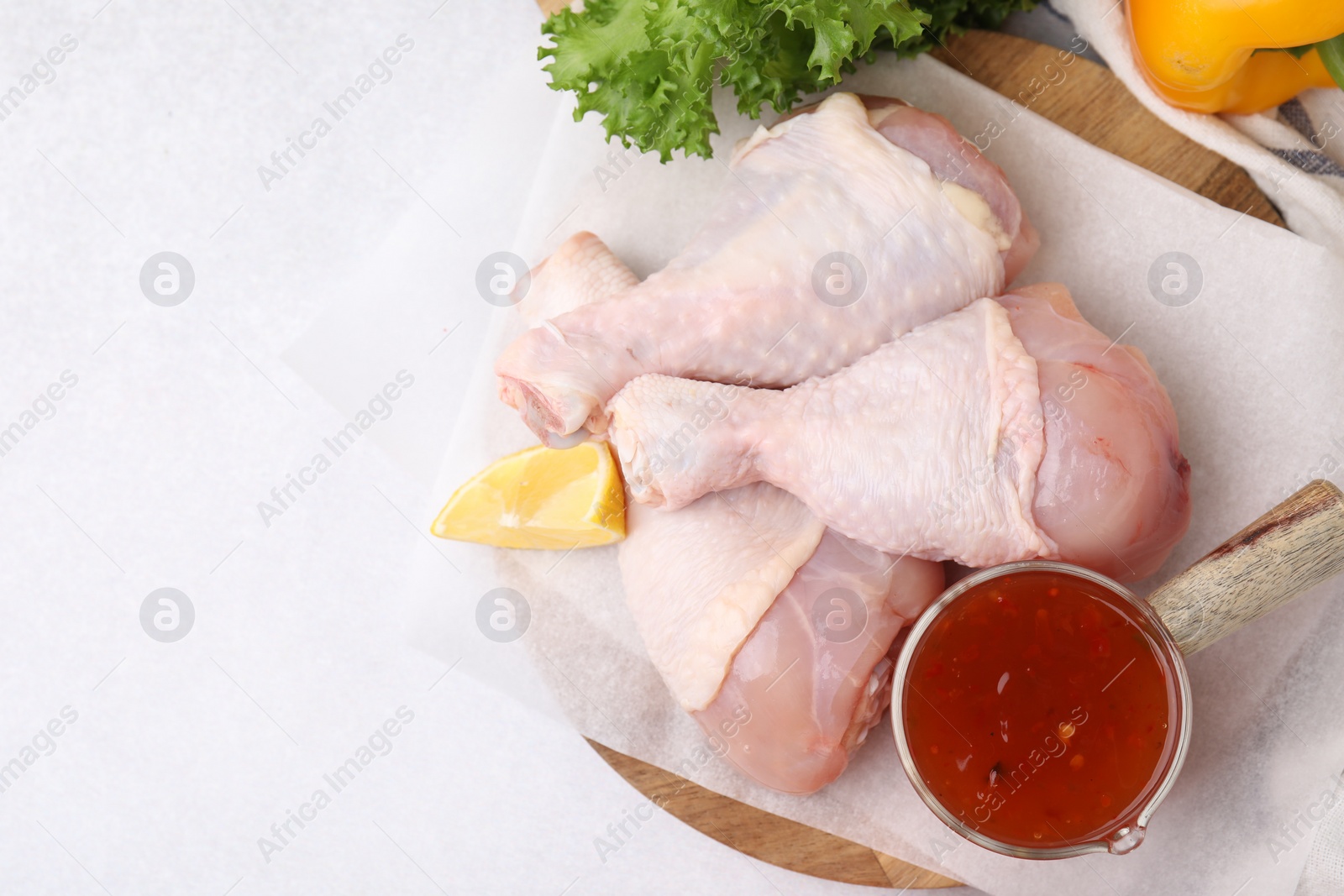 Photo of Fresh marinade, raw chicken drumsticks and lemon on white table, flat lay. Space for text