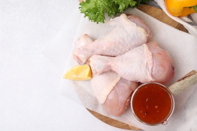 Photo of Fresh marinade, raw chicken drumsticks and lemon on white table, flat lay. Space for text