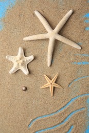 Photo of Beautiful starfishes and sand on blue background, flat lay