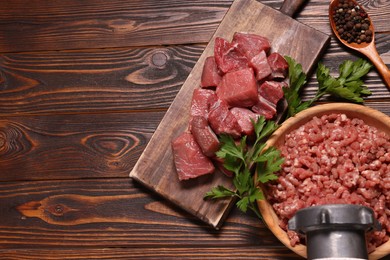 Photo of Manual meat grinder with beef, peppercorns and parsley on wooden table, above view. Space for text