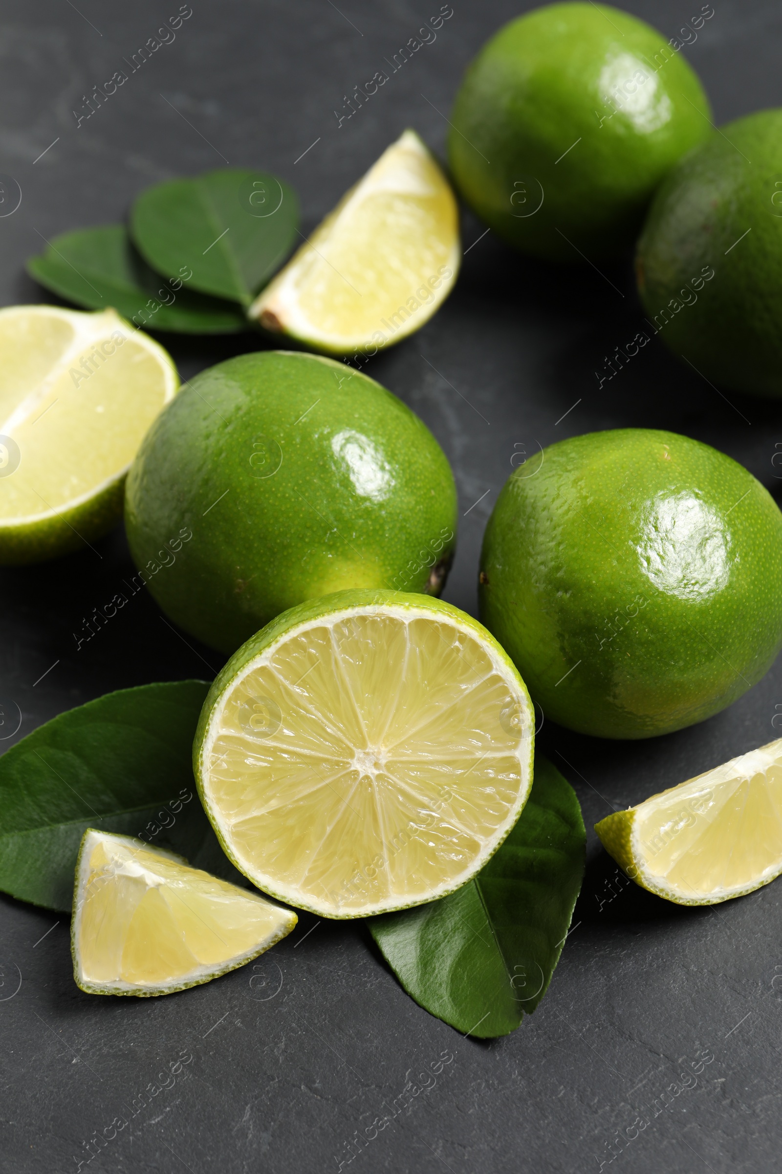 Photo of Fresh ripe limes and leaves on black table, closeup