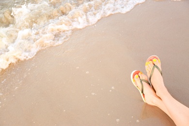 Photo of Closeup of woman with stylish flip flops on sand near sea, space for text. Beach accessories