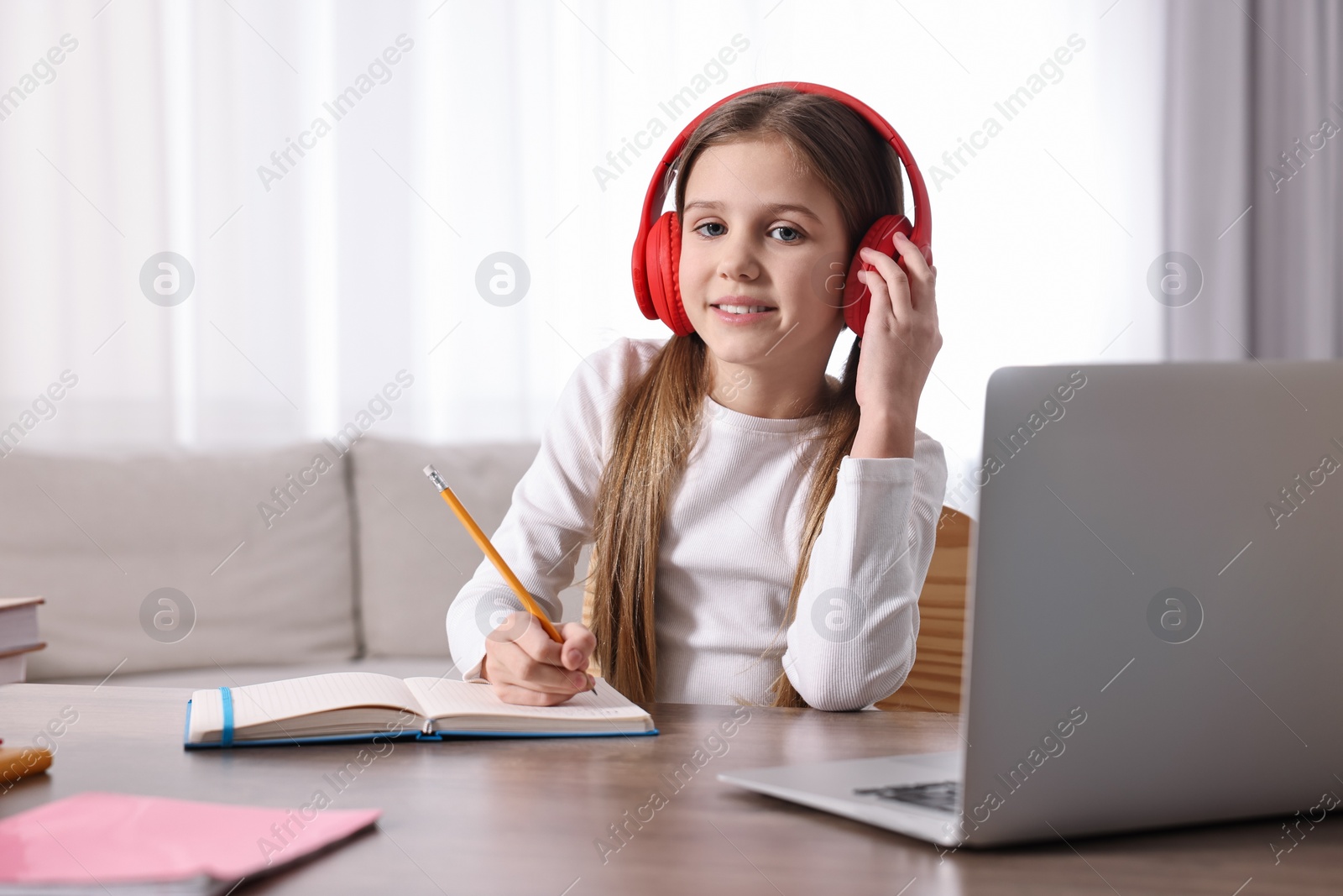 Photo of E-learning. Cute girl taking notes during online lesson at table indoors