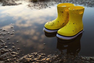 Photo of Yellow rubber boots in puddle outdoors, space for text. Autumn walk