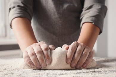 Man kneading dough at table in kitchen, closeup