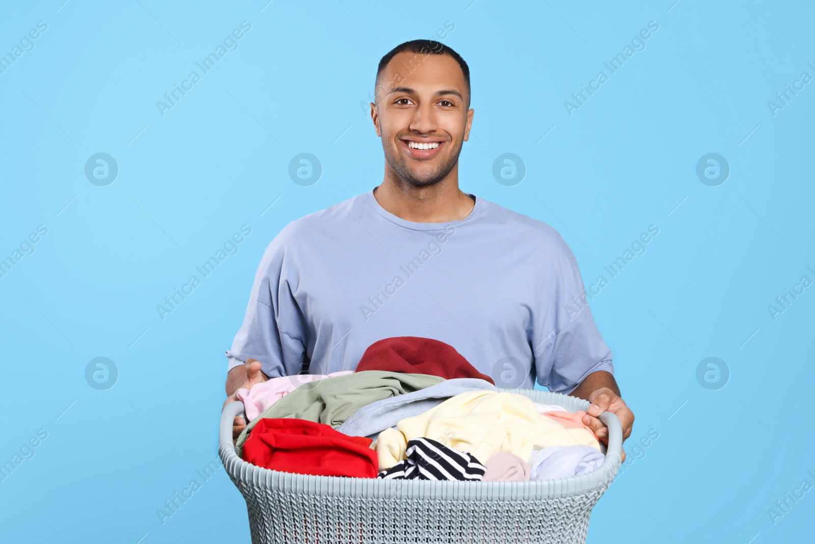 Photo of Happy man with basket full of laundry on light blue background