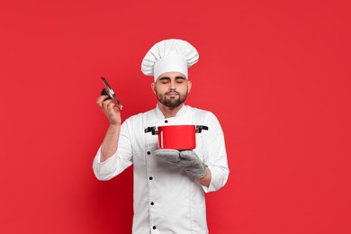 Professional chef smelling something in cooking pot on red background