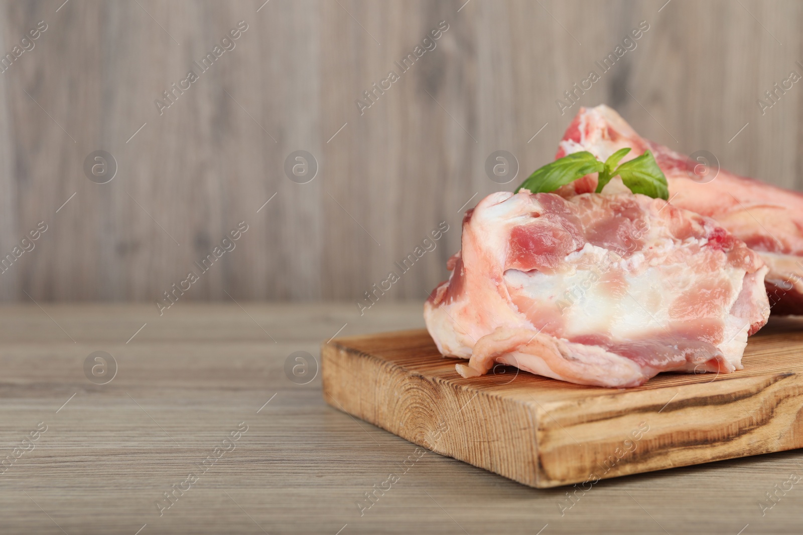 Photo of Cutting board with raw chopped meaty bones and basil on wooden table. Space for text