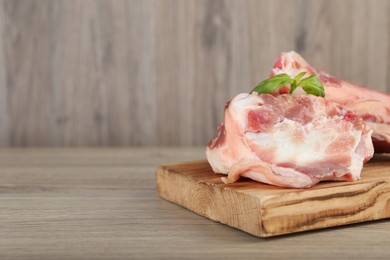 Photo of Cutting board with raw chopped meaty bones and basil on wooden table. Space for text