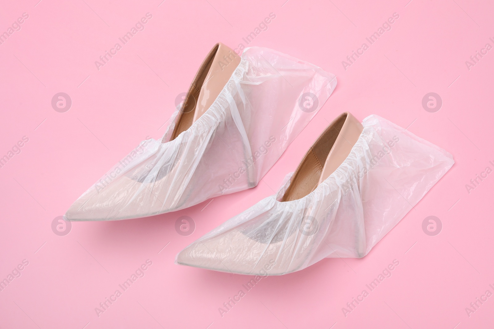 Photo of High heels in shoe covers on pink background, top view