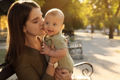 Young mother with her cute baby on bench in park