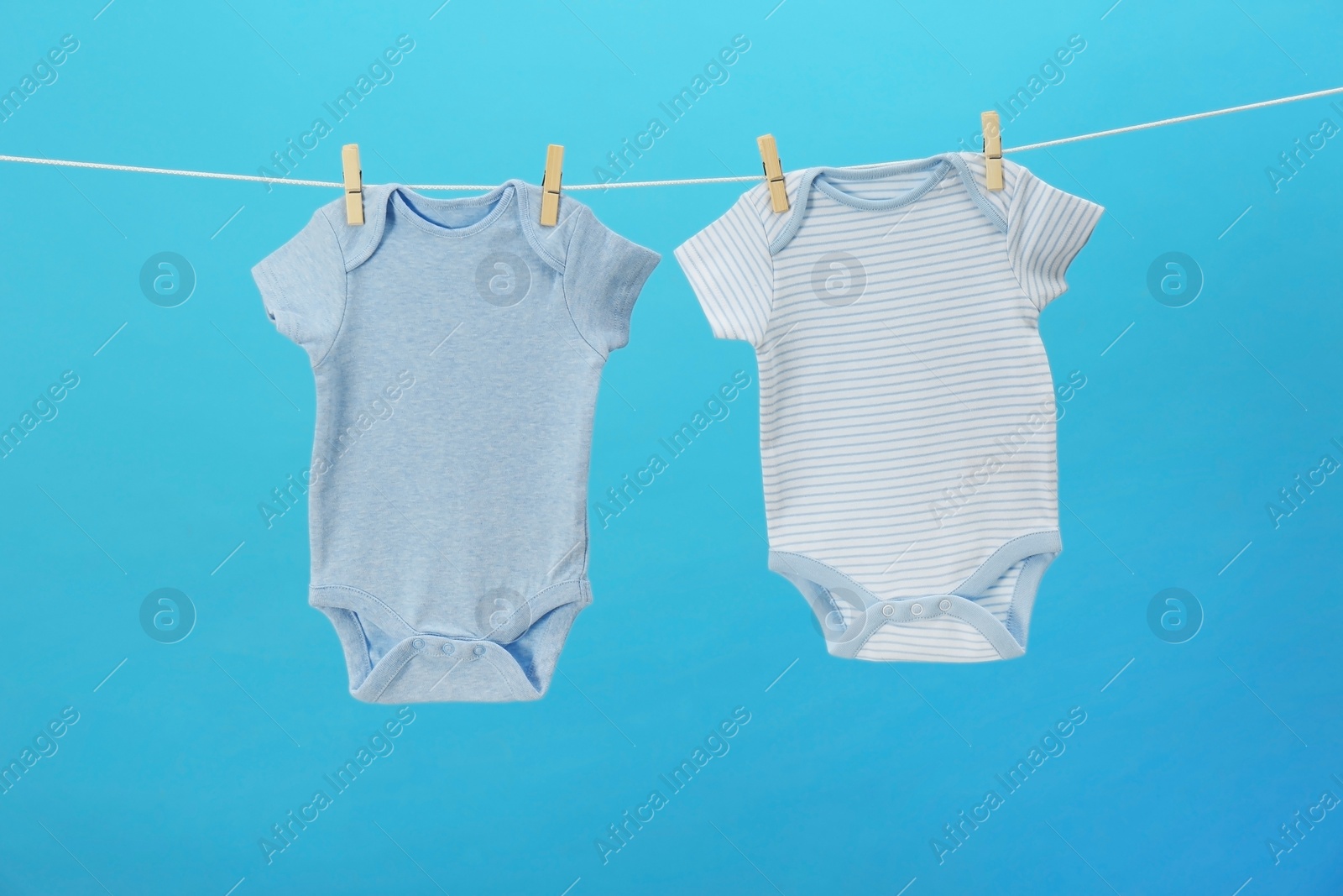 Photo of Baby onesies hanging on clothes line against blue background. Laundry day