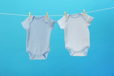 Photo of Baby onesies hanging on clothes line against blue background. Laundry day