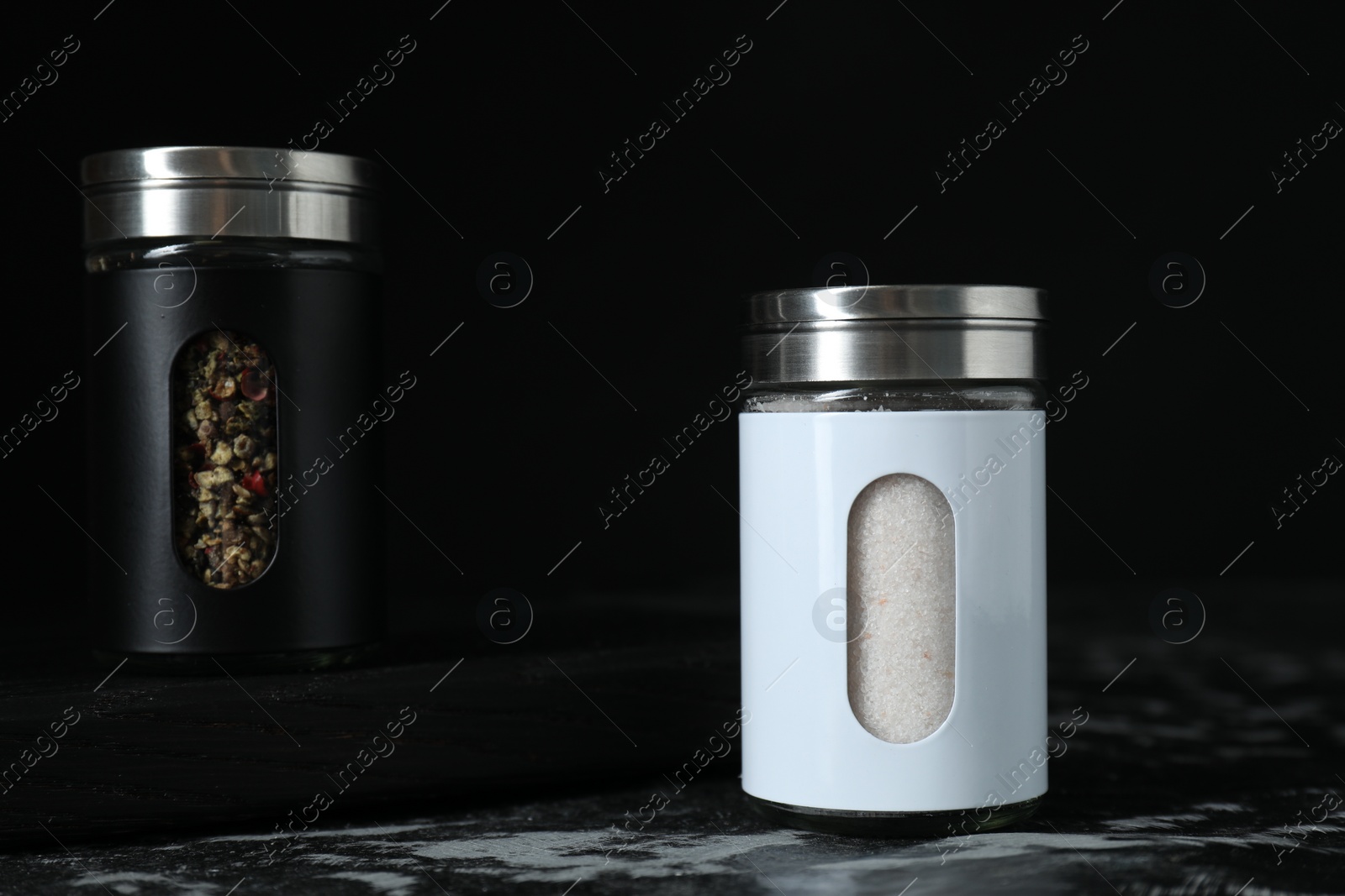 Photo of Salt and pepper shakers on dark table against black background