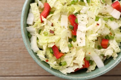 Photo of Tasty salad with Chinese cabbage, bell pepper and green onion in bowl on wooden table, top view