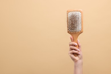 Photo of Woman holding brush with lost hair on beige background, closeup and space for text. Alopecia problem
