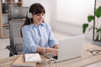 Woman in headphones watching webinar at wooden table in office