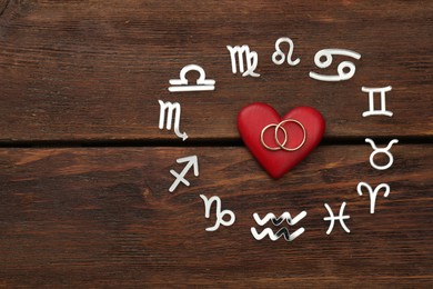 Zodiac signs, red heart and wedding rings on wooden background, flat lay. Space for text