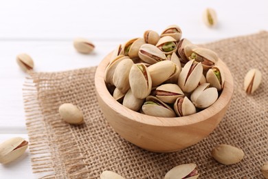 Tasty pistachios in bowl on white wooden table