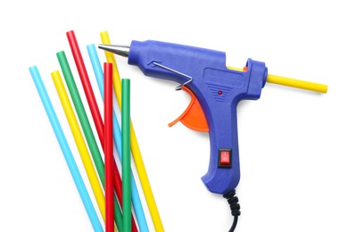 Photo of Blue glue gun and colorful sticks on white background, top view